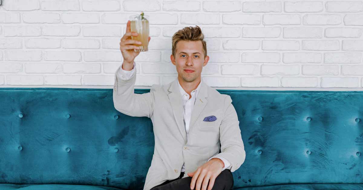 Young man sitting on a couch holding up a drink